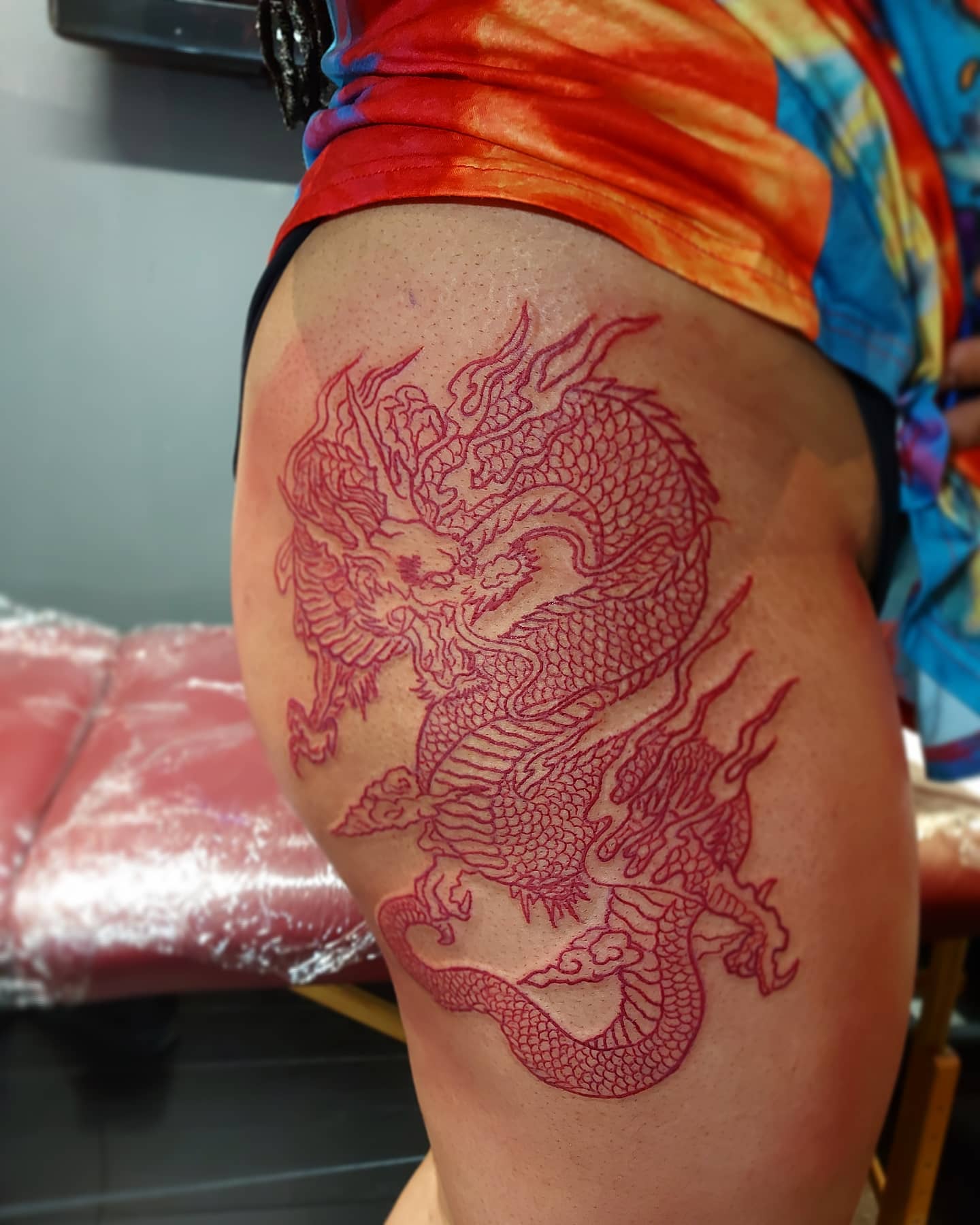 Red linework dragon tattoo on a thigh by Jamie Brown at Raro Tattoo